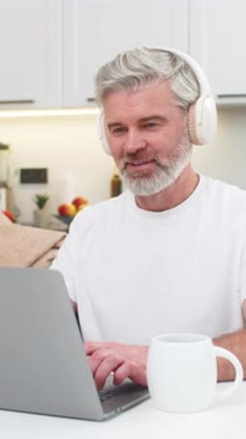 Middleaged Man Works on Laptop Smiles Enjoys Music in Headphones Drinks Coffee Relaxes Focus Calm