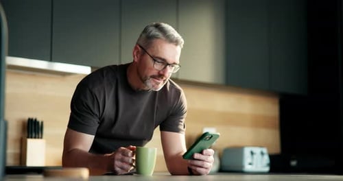 Man Drinking Coffee Uses Phone in Modern Kitchen