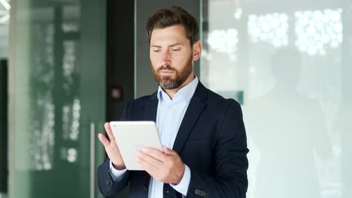 Handsome businessman in formal suit is using digital tablet standing in business office. Worker read