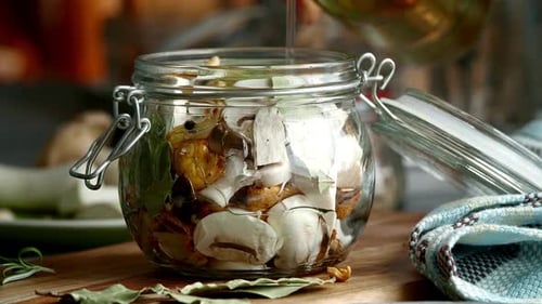 Pouring Oil into a Glass Jar with Sliced Mushrooms and Herbs