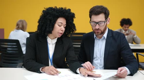 Hombre caucásico y mujer afroamericana discuten el informe financiero en la oficina