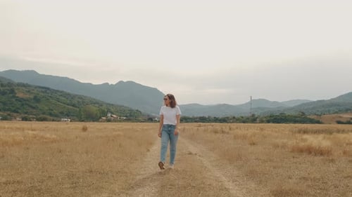 A Woman Strolls Leisurely Through a Tranquil Green Field Basking Under a Stunning Sky