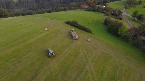 Aerial view of agricultural machinery harvesting crops in hilly landscape.