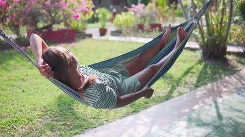 Woman is resting in hammock and enjoying summer in garden
