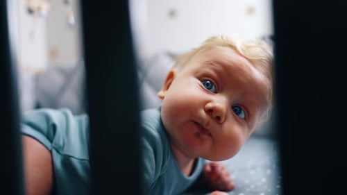Cute chubby face of a cute Caucasian infant. Close up. Adorable baby lying in the crib on his belly.