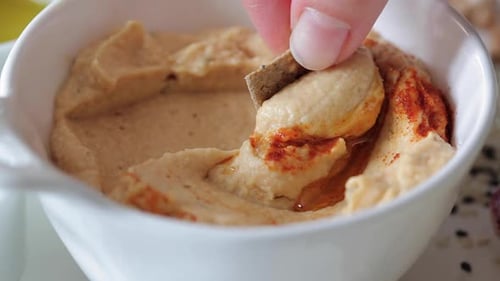 Dipping Cracker into Bowl of Homemade Hummus