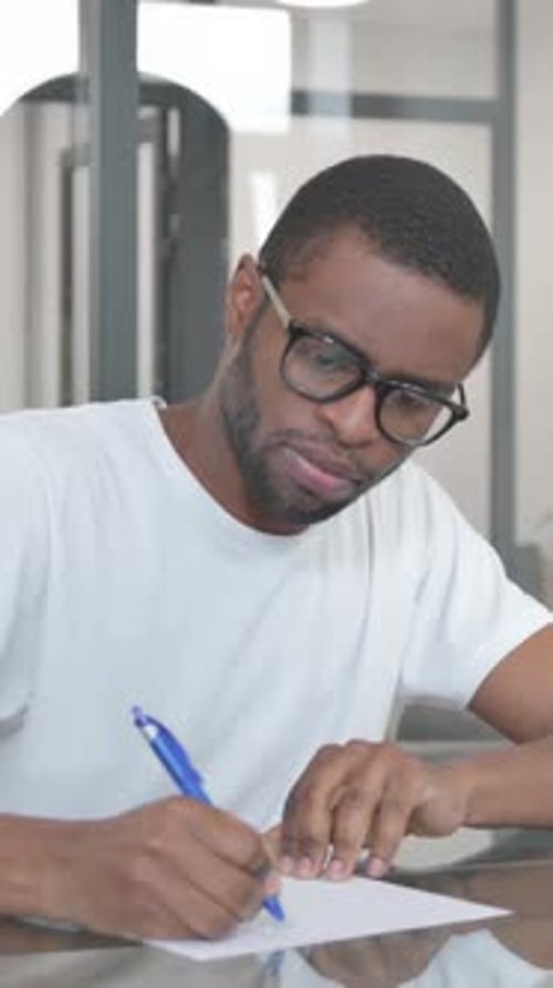Young African Man Writing a Letter in Office, vertical video
