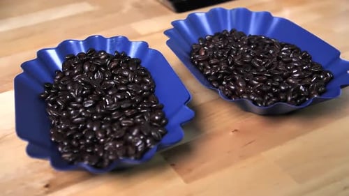 Shiny coffee beans in two blue bowls, slow motion circle shot
