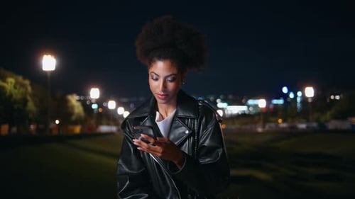 Woman Using Mobile Phone at Night in City Park