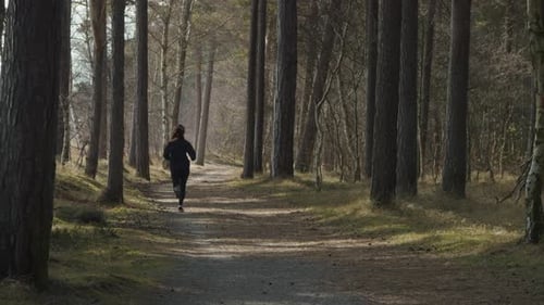 Fitness healthy jogger woman runs along forrest trail away from the camera towards background. Fit y
