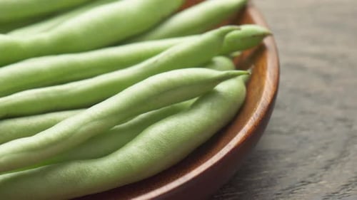 Closeup view of fresh green beans on wooden plate