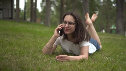 A Young Woman Lies on the Grass in the Park and Chats on the Phone Girl on the Grass with a Phone in