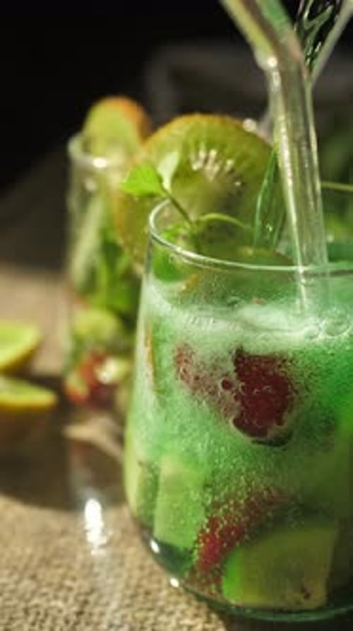 Vertical Soda is Slowly Poured Into a Glass with Strawberries and Kiwi with the Addition of Green