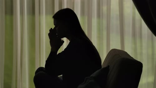Silhouette of a Distressed Woman in Front of Backlit Curtains