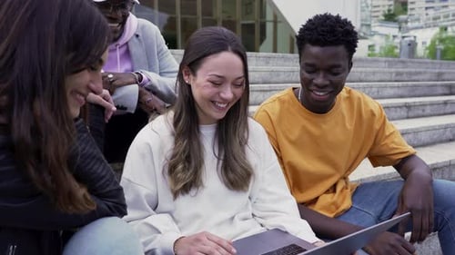 College Students Having Fun While Sitting On Stairs And Looking At The Laptop In University. medium