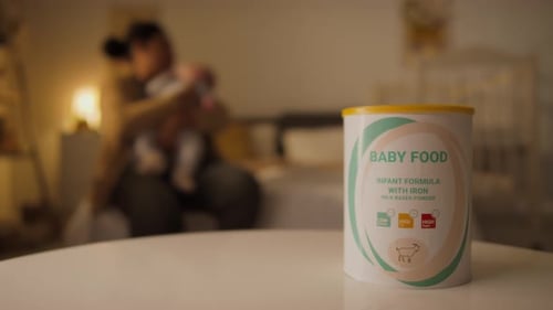 Tin of Baby Milk Formula on Table in Bedroom and Anonymous Mother Cuddling Baby