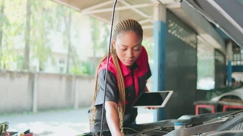 A black female automotive mechanical worker checks EV car at a fixing garage.