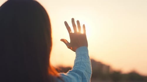 Silhouette: Die Hand einer glücklichen Frau streckt sich bis zur goldenen Stunde des Sonnenuntergangs aus