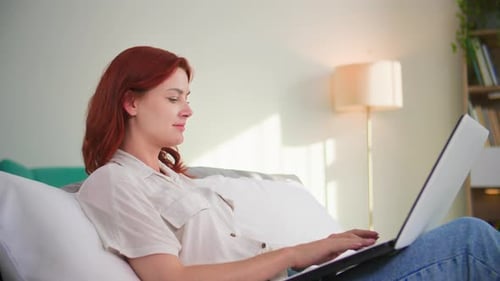 Woman Using Laptop Relaxing on Couch at Home