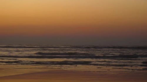 Silhouette of a man walking on a beach during the sunset.