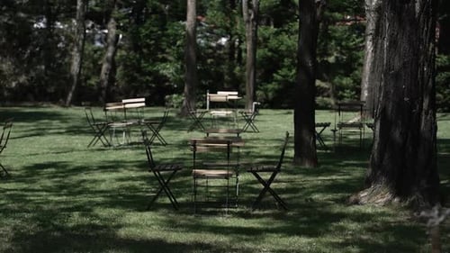 Empty outdoor seating area with scattered tables and chairs in a shaded, wooded garden