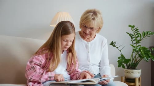 Girl Reads Book with Senior Woman on Sofa
