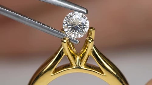 Juwelierpinzette, die einen funkelnden Diamanten in eine Goldringfassung legt