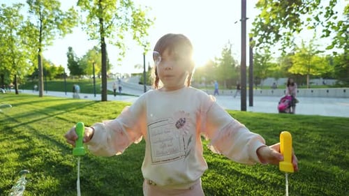 A Little Girl with Soap Bubbles on the Green Grass in the Park