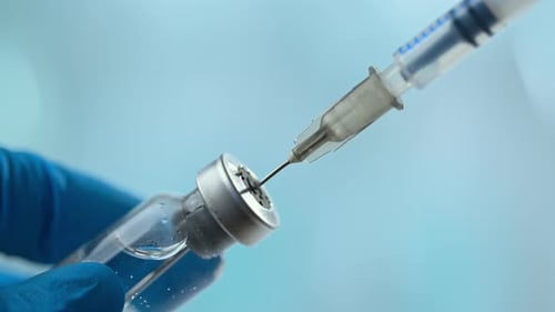 Doctor's hand holding glass vial and take injection with syringe over blue background.