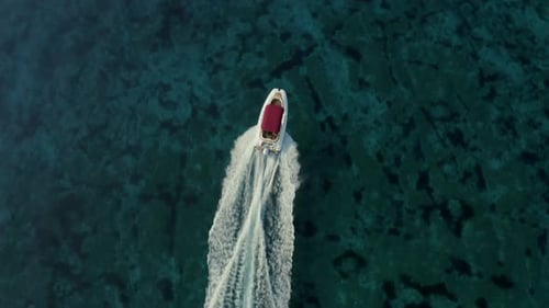 Slow motion, aerial shot over speed boat with a red roof top passing through clear turquoise sea.