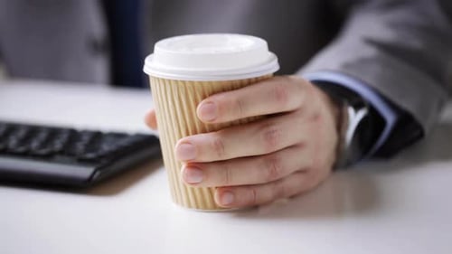 Geschäftsmann hält Einweg-Kaffeetasse in der Pause am Büroarbeitsplatz in der Hand