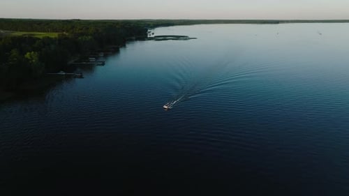 orbiting drone shot of a pontoon with a small wake on a lake at sunset