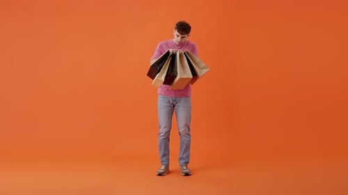 Excited Man Holding Shopping Bags on Orange Background