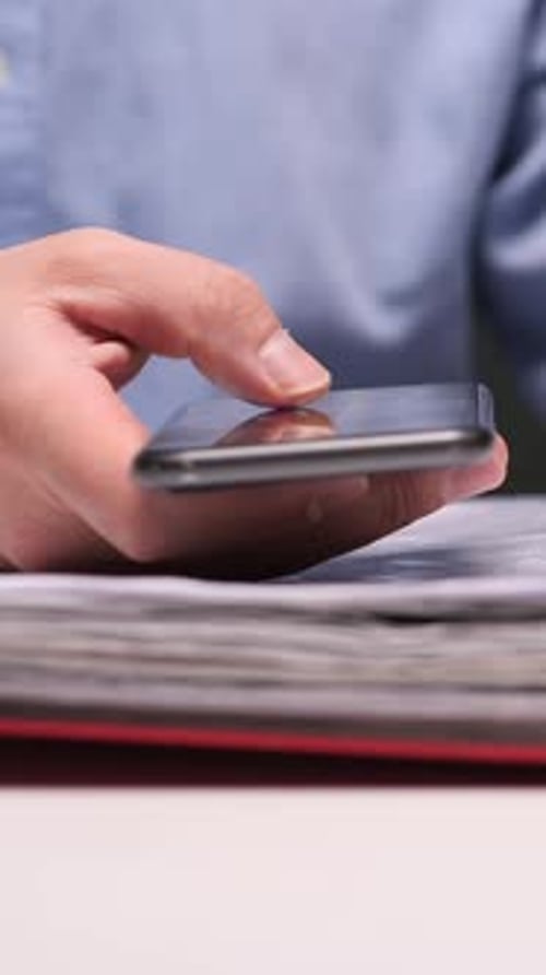 Hand Taps Cellphone On Stack Of Paperwork