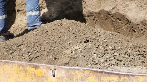 Worker Shoveling Soil Into Container on Bright Day