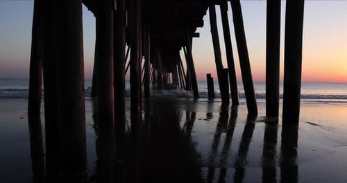 Blick in Zeitlupe bei Sonnenaufgang auf Wellen, die heranrollen und gegen die Holzstützen eines Fischers prallen p