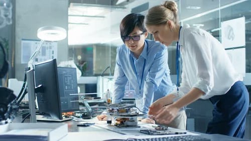 Two Computer Engineers Choose Printed Circuit Boards to Work with. In The Background Technologicall