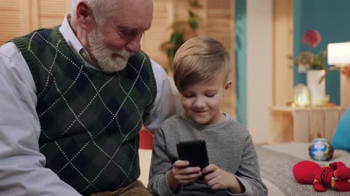 Grandfather watches grandson use mobile phone indoors