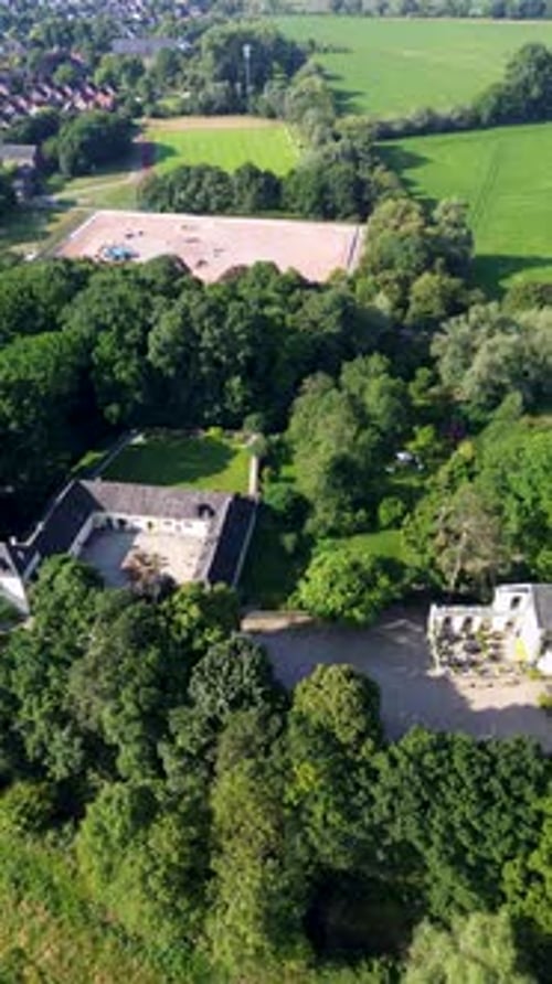 A charming historic estate with a U-shaped courtyard, surrounded by lush greenery, fields, and trees