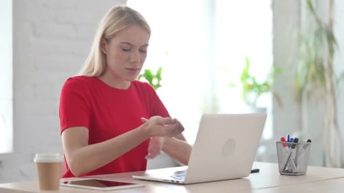 Young Blonde Woman having Wrist Pain while using Laptop in Office