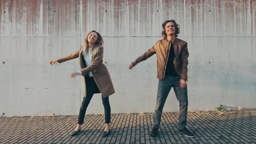 Cheerful Girl and Happy Young Man with Long Hair are Actively Dancing Meme Moves on a Street next t