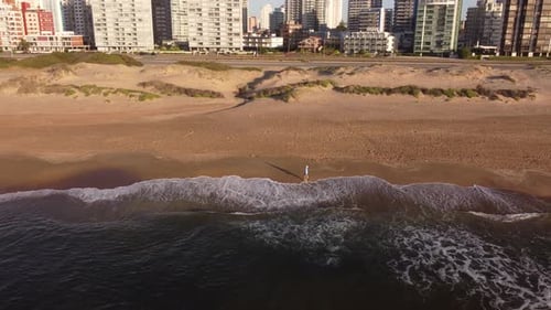 Homem caminhando na praia ao nascer do sol com a cidade ao fundo, Punta del Este, no Uruguai. Panorâmica aérea