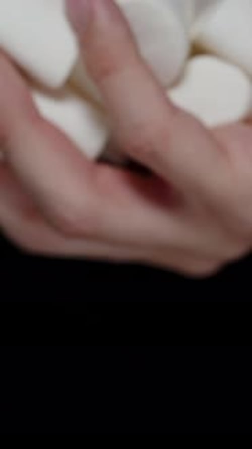 Vertical video. Hand Slowly Pouring White Marshmallows Against a Black Background. Slow Motion.