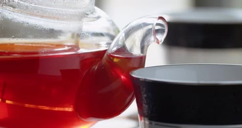 Plan rapproché du versement du thé d'une théière en verre dans une tasse en céramique