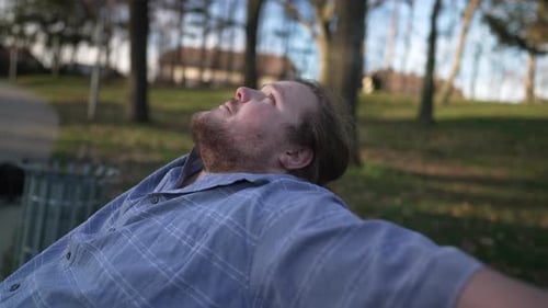 Meditative young man sitting at park bench enjoying nature outdoors