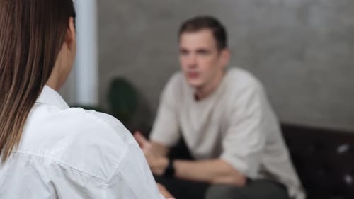 Woman in White Shirt Talking to Man on Sofa