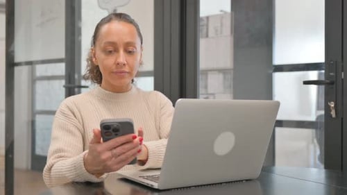 Woman Works On Laptop While Holding Smartphone