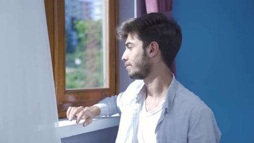 Man Smiling and Looking Out Window in Apartment