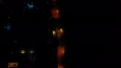 Drone flies over empty road in nighttime city.