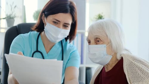 Doctor Reviewing Paperwork With Senior Woman in Mask